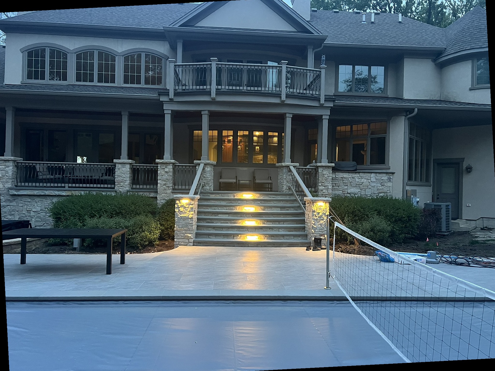 Stone-trimmed Naperville home exterior with patio, balcony and landscape lighting illuminated at dusk