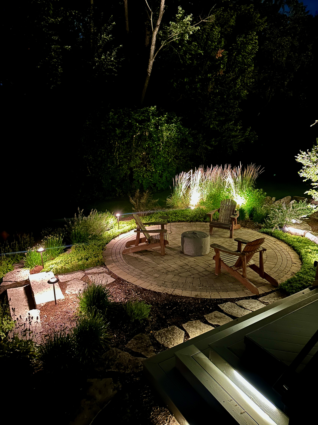Naperville backyard fire pit and paver patio lit at night with landscape lighting
