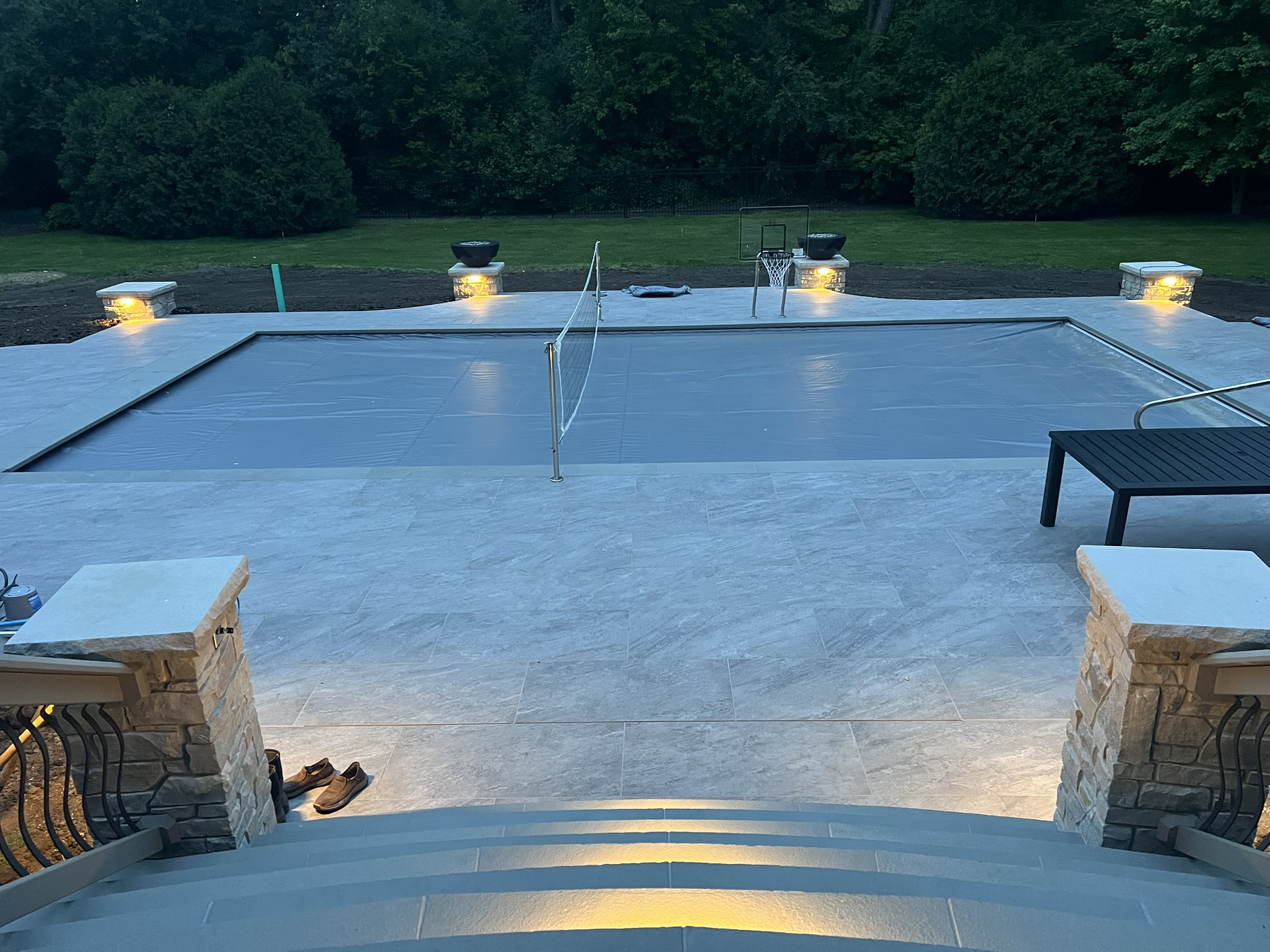 Backyard pool with automated cover, fire bowls and landscape lighting glowing at dusk in Naperville